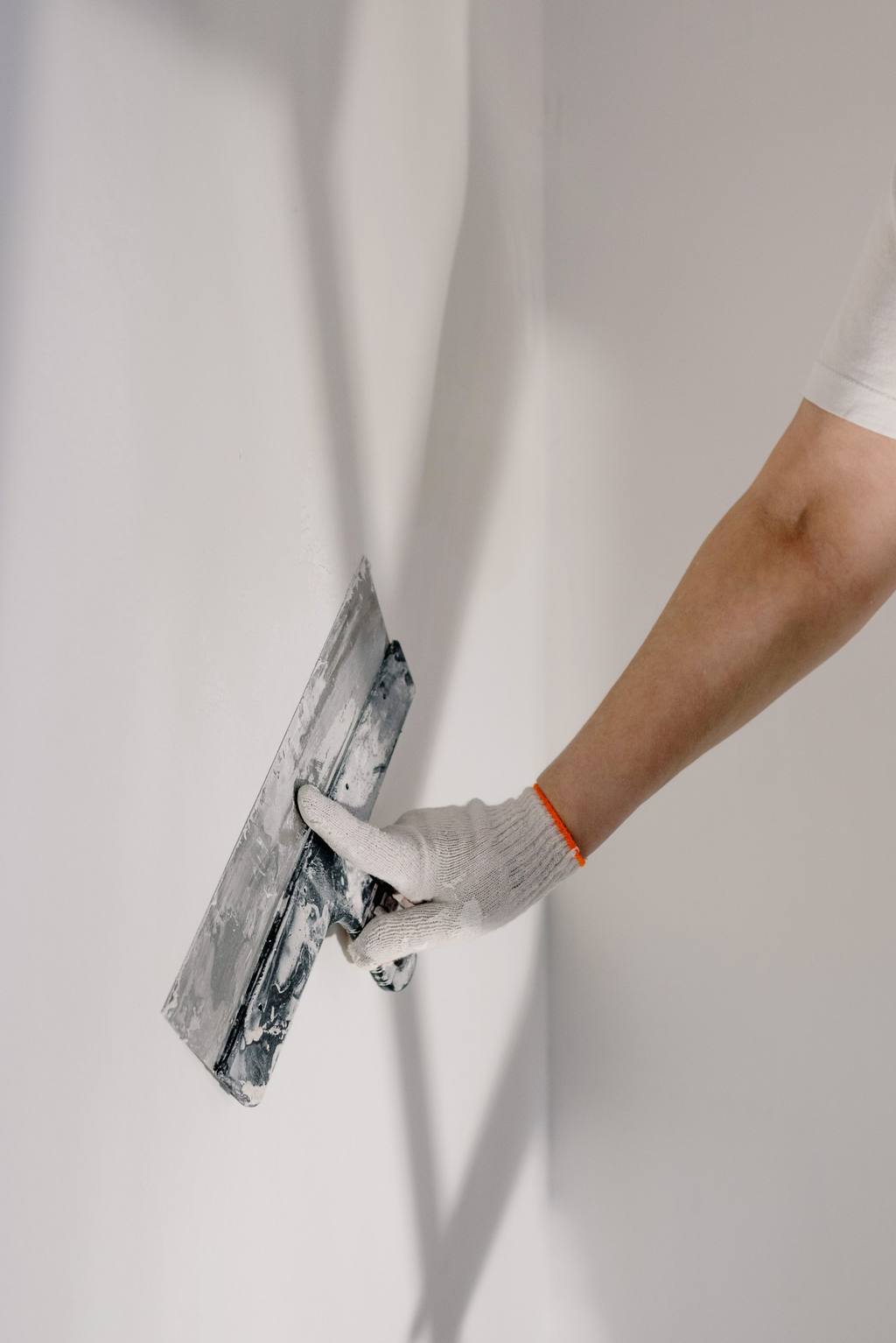 Plasterer’s gloved hand smoothing a wall with a trowel